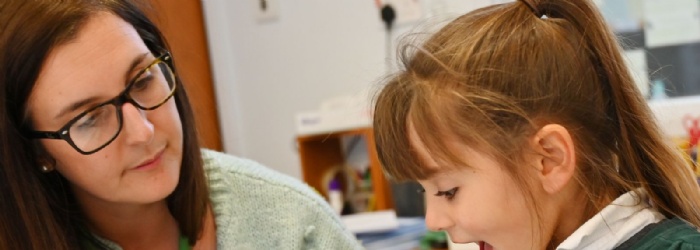 Student sitting at table being taught by a teacher